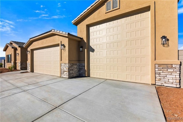 exterior space featuring a garage, stone siding, driveway, and stucco siding