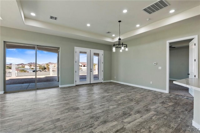 spare room with a tray ceiling, visible vents, baseboards, and wood finished floors