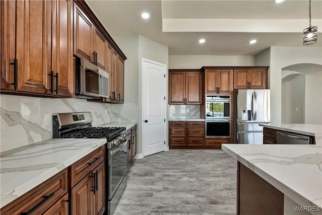 kitchen featuring brown cabinetry, light stone countertops, stainless steel appliances, pendant lighting, and recessed lighting