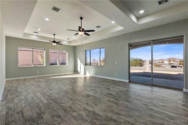 spare room featuring a raised ceiling, visible vents, baseboards, and wood finished floors