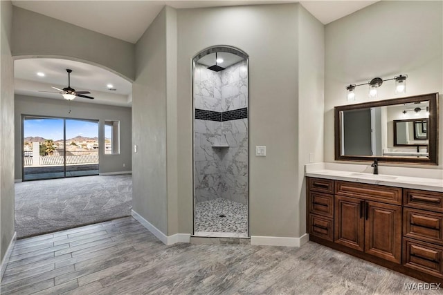 bathroom with wood finished floors, a ceiling fan, vanity, baseboards, and a marble finish shower