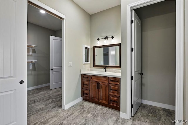 bathroom featuring baseboards, a walk in closet, wood finished floors, and vanity