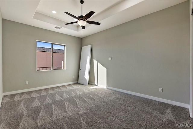 empty room featuring visible vents, baseboards, a raised ceiling, a ceiling fan, and light colored carpet