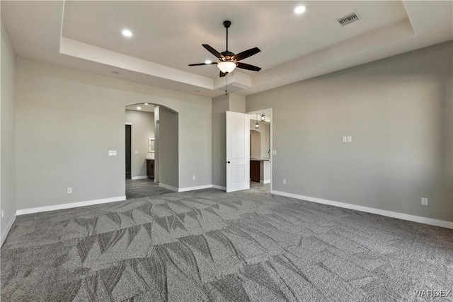 unfurnished bedroom featuring arched walkways, visible vents, baseboards, carpet, and a raised ceiling