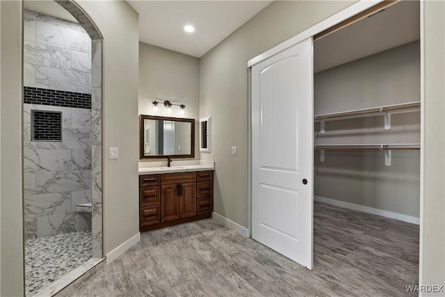 bathroom with a walk in closet, tiled shower, vanity, and baseboards