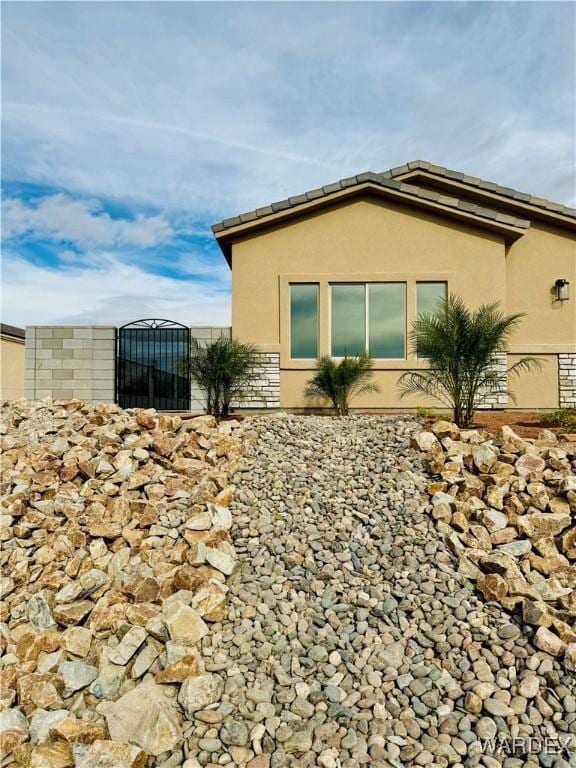 view of home's exterior with stone siding, a gate, fence, and stucco siding