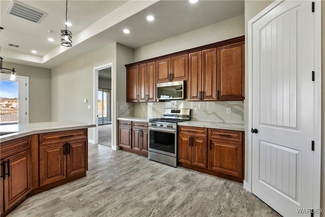 kitchen featuring pendant lighting, light wood finished floors, stainless steel appliances, tasteful backsplash, and visible vents