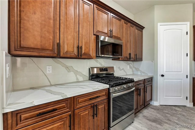 kitchen featuring light stone counters, stainless steel appliances, backsplash, brown cabinetry, and light wood-type flooring