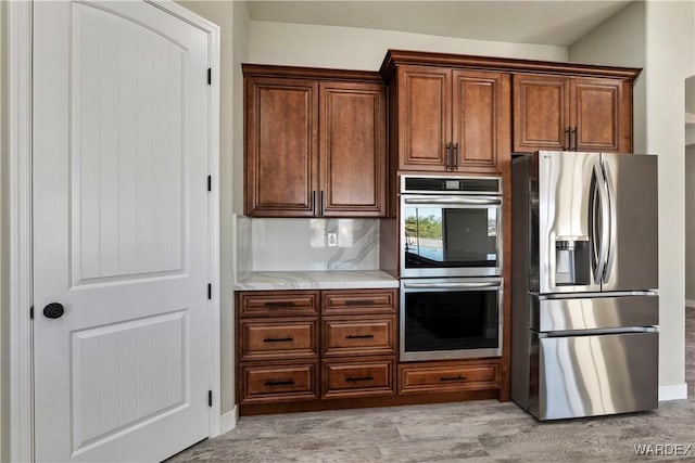 kitchen with light wood-type flooring, light stone countertops, stainless steel appliances, and decorative backsplash