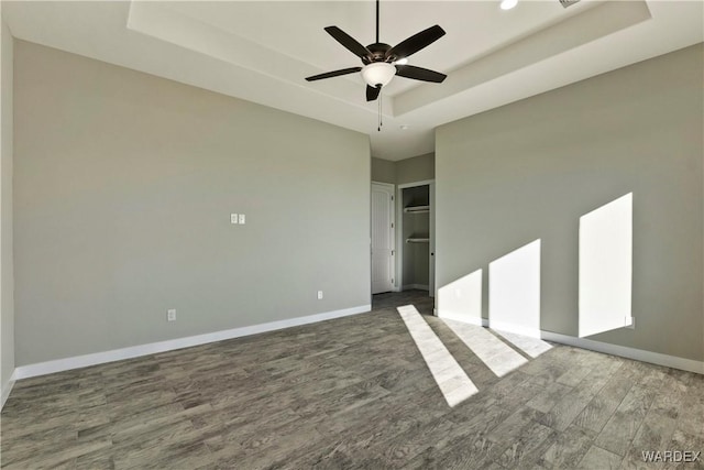 unfurnished bedroom featuring dark wood-type flooring, a ceiling fan, baseboards, a closet, and a raised ceiling