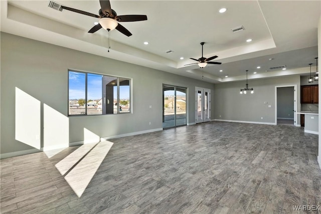 unfurnished living room with a tray ceiling, visible vents, and wood finished floors