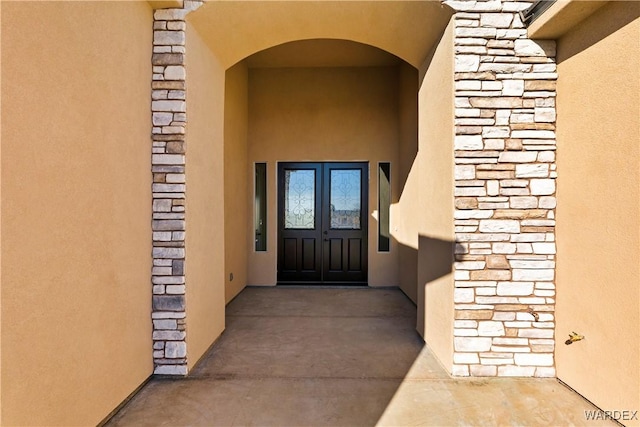 property entrance with stone siding, stucco siding, and french doors