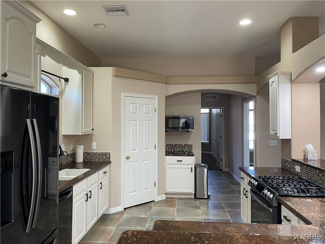 kitchen with visible vents, arched walkways, dark stone countertops, black appliances, and white cabinetry