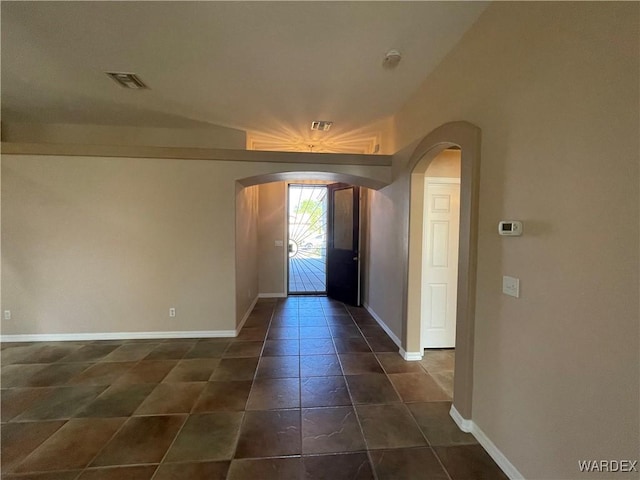 foyer entrance with arched walkways, dark tile patterned flooring, visible vents, and baseboards