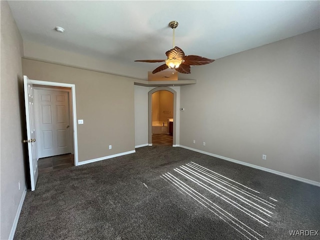 unfurnished bedroom featuring arched walkways, dark colored carpet, ceiling fan, and baseboards