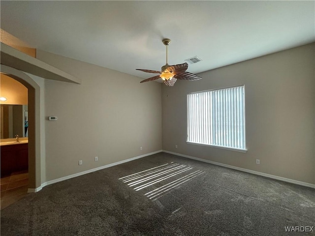 spare room with arched walkways, dark colored carpet, visible vents, a ceiling fan, and baseboards