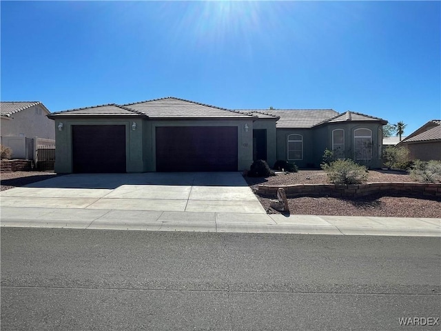 view of front facade featuring an attached garage, a tile roof, concrete driveway, and stucco siding