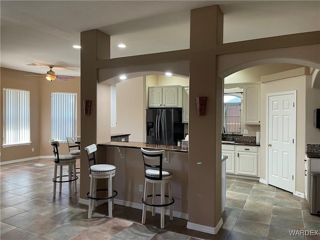 kitchen featuring dark countertops, white cabinets, arched walkways, and black fridge