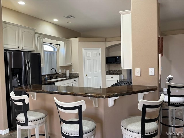 kitchen with a peninsula, black appliances, white cabinetry, and a breakfast bar