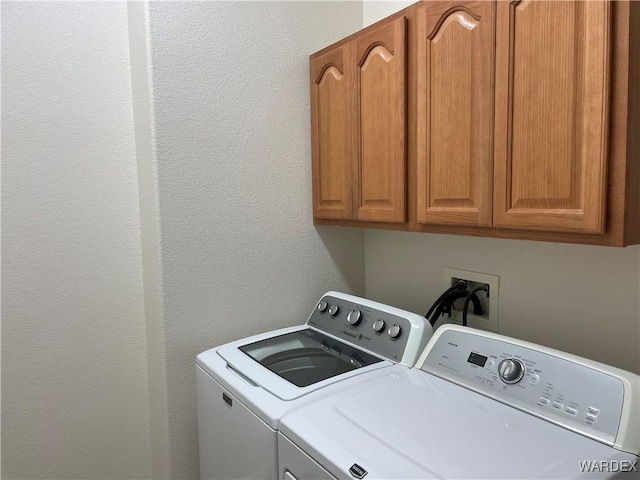 laundry area featuring a textured wall, washing machine and clothes dryer, and cabinet space