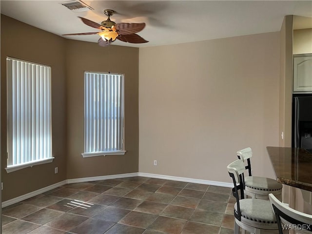 unfurnished dining area featuring dark tile patterned flooring, visible vents, ceiling fan, and baseboards