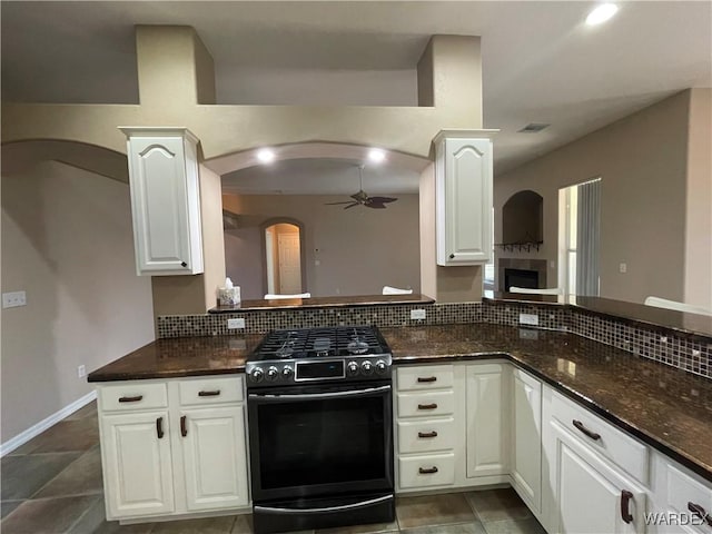 kitchen with tasteful backsplash, dark stone counters, stainless steel gas stove, and white cabinetry