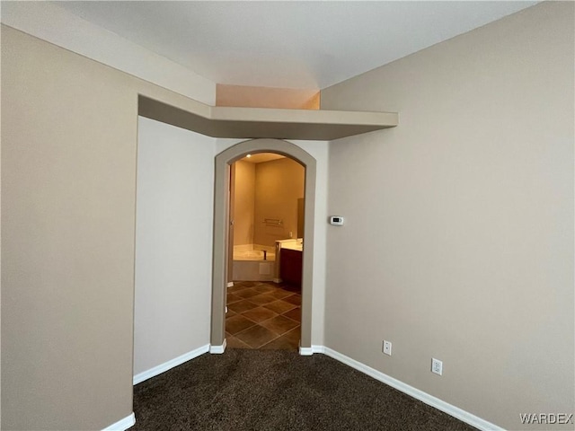 empty room featuring arched walkways, dark carpet, and baseboards