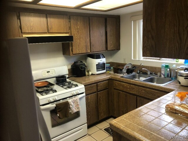 kitchen featuring dark brown cabinetry, white gas range oven, tile counters, range hood, and a sink