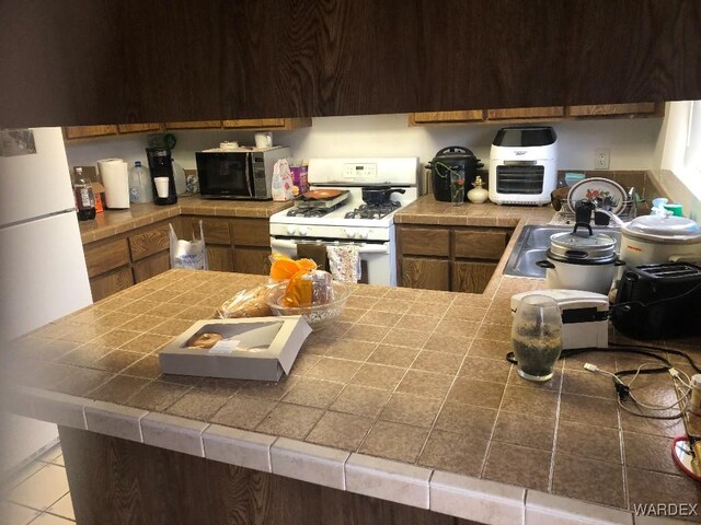 kitchen with light tile patterned floors, tile countertops, white gas range, black microwave, and a sink