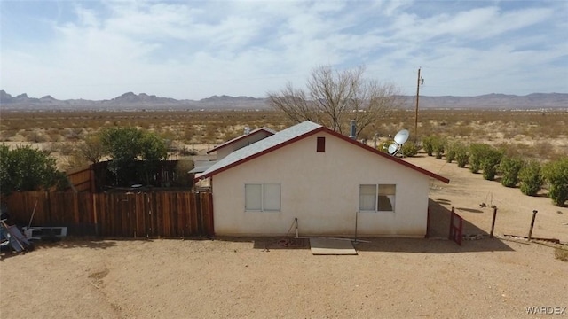 view of side of home with fence, a mountain view, and stucco siding