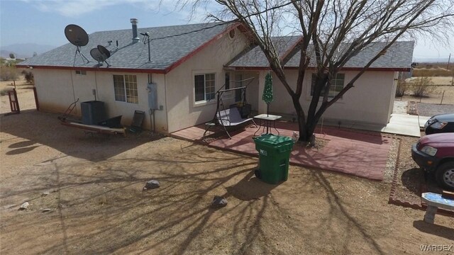 back of house featuring roof with shingles, stucco siding, a patio, and central air condition unit