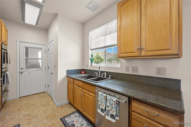 kitchen featuring dark countertops, baseboards, dishwasher, brown cabinetry, and a sink