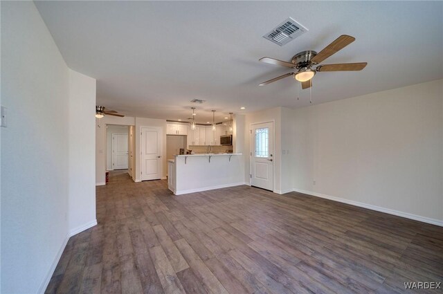 unfurnished living room with ceiling fan, dark wood-type flooring, visible vents, and baseboards