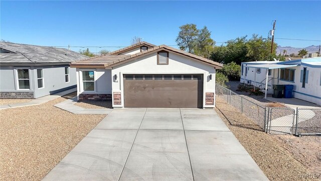 view of front of property featuring an attached garage, fence, driveway, stone siding, and stucco siding