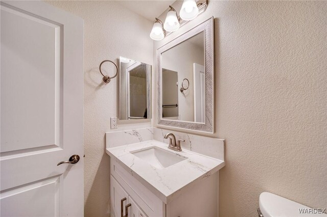 half bathroom featuring toilet, a textured wall, and vanity