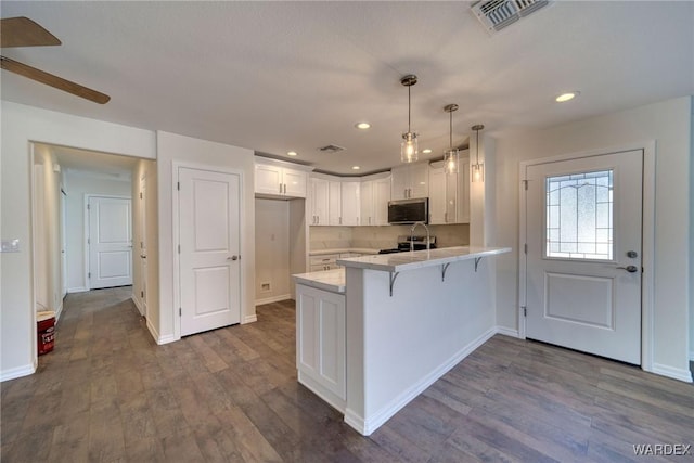 kitchen with white cabinets, stainless steel microwave, dark wood-style flooring, a peninsula, and light countertops