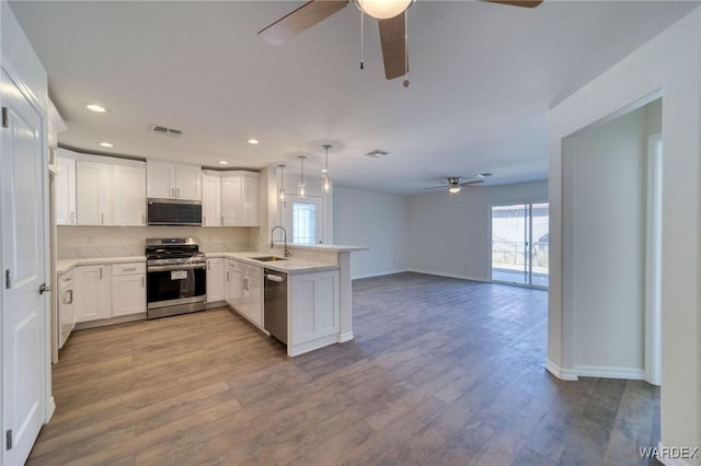 kitchen featuring stainless steel appliances, a peninsula, wood finished floors, a sink, and light countertops