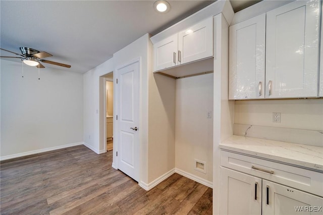 kitchen with light stone counters, wood finished floors, a ceiling fan, baseboards, and white cabinets