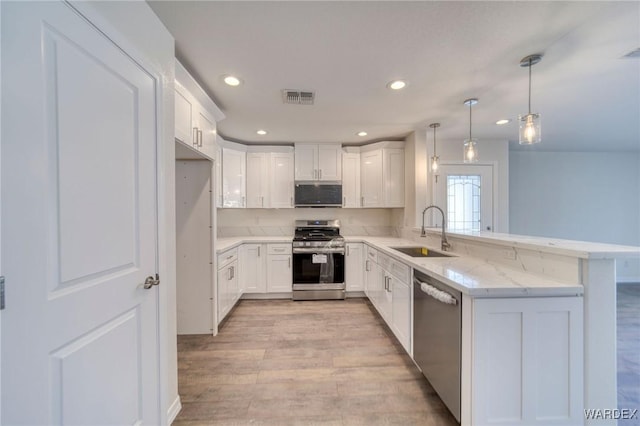 kitchen with stainless steel appliances, a peninsula, a sink, visible vents, and light wood-style floors