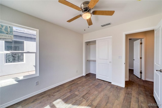 unfurnished bedroom with a closet, visible vents, a ceiling fan, wood finished floors, and baseboards