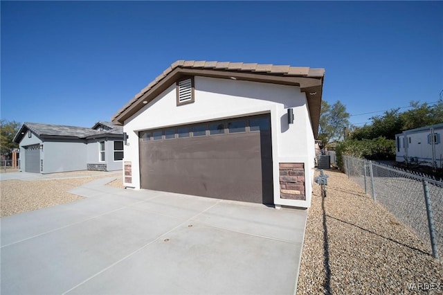 exterior space featuring stucco siding, concrete driveway, central AC, fence, and a garage