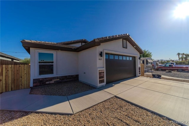 view of front of house with a garage, fence, concrete driveway, stone siding, and stucco siding