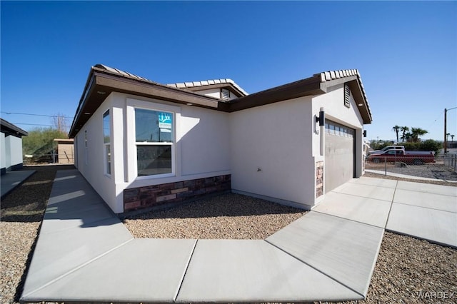 view of property exterior with a garage, driveway, stone siding, fence, and stucco siding