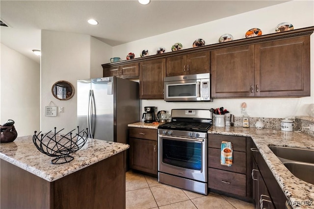 kitchen featuring light tile patterned floors, appliances with stainless steel finishes, a sink, dark brown cabinets, and light stone countertops