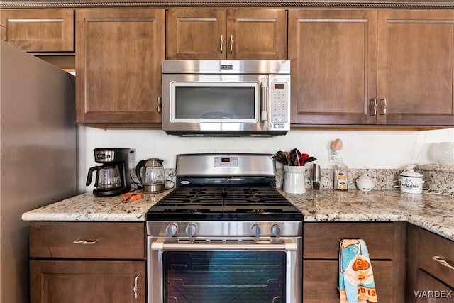 kitchen featuring stainless steel appliances, light stone counters, and brown cabinetry