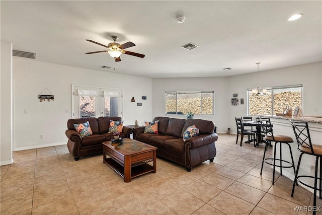 living room featuring light tile patterned flooring, baseboards, visible vents, and ceiling fan with notable chandelier