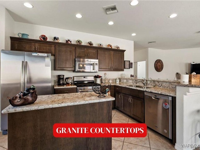 kitchen featuring light tile patterned floors, stainless steel appliances, a peninsula, a sink, and visible vents