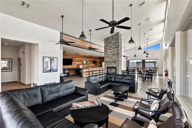 living area with wood walls, light wood-type flooring, a towering ceiling, and visible vents