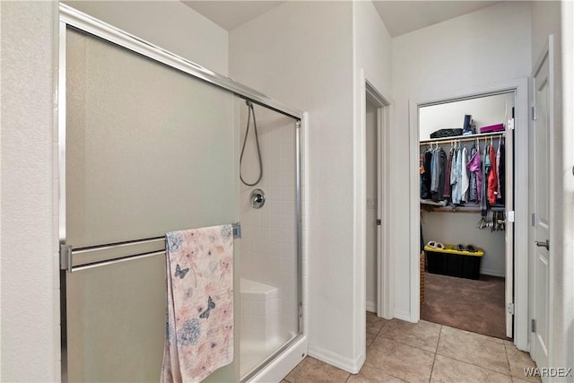 bathroom with a stall shower, a walk in closet, tile patterned flooring, and baseboards