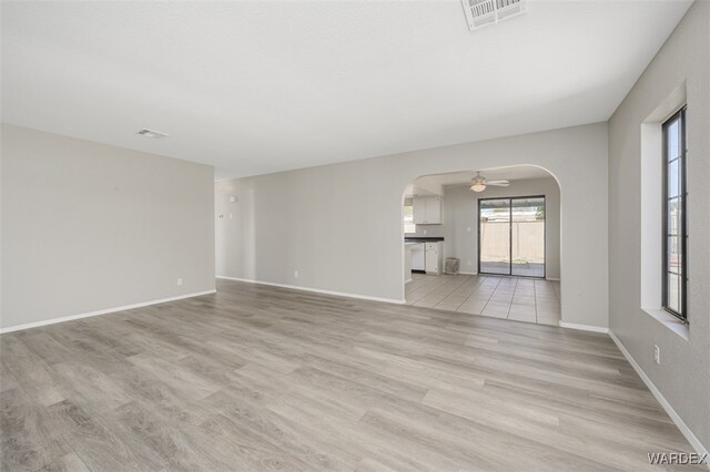 spare room featuring light wood finished floors, visible vents, arched walkways, and baseboards